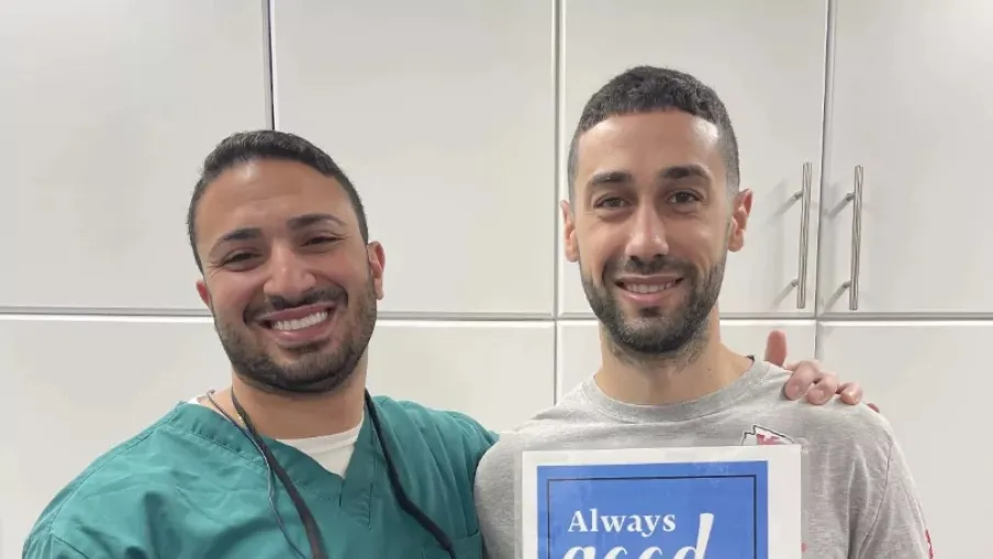 Smiling dentist in scrubs with patient holding a sign reading Always good fillings here.