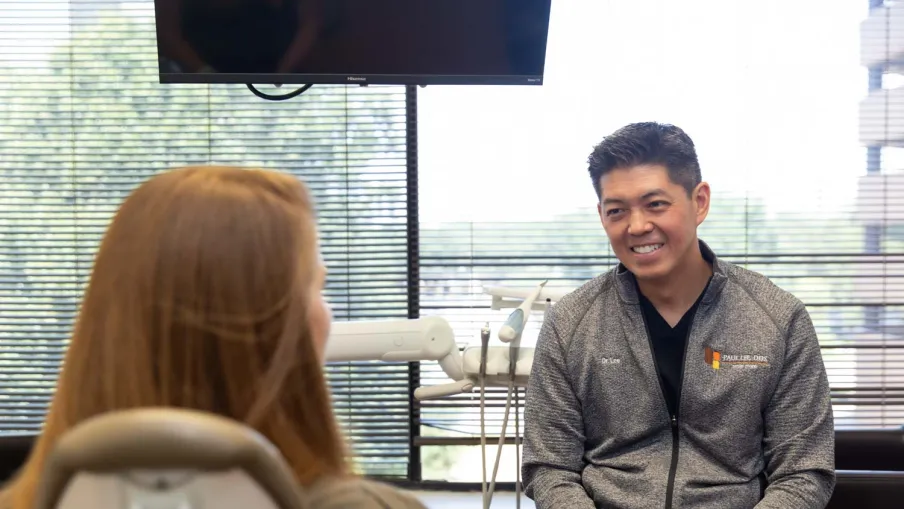 Dentist in gray jacket talking and smiling with female patient in modern dental office with equipment