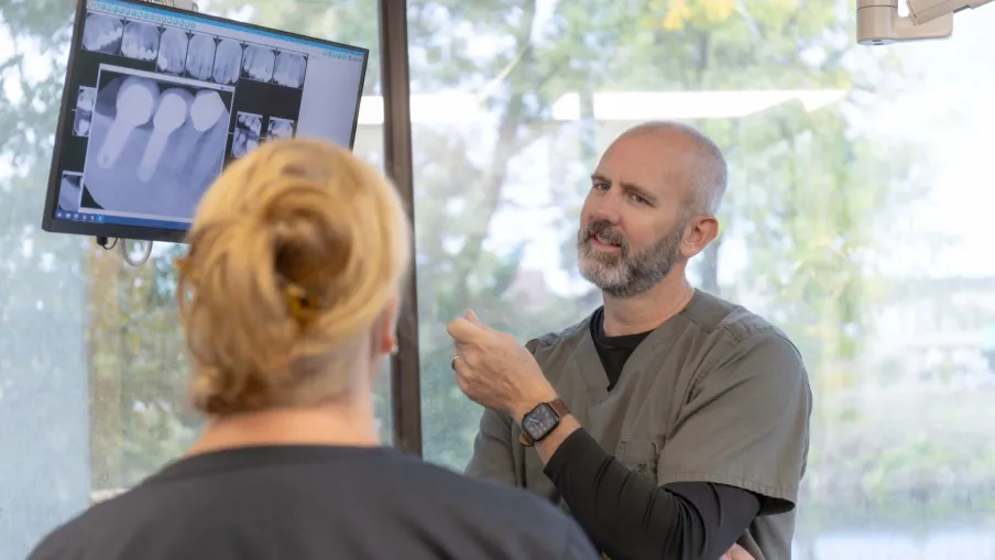 Dentist explaining dental X-rays to patient in modern clinic with large window background.