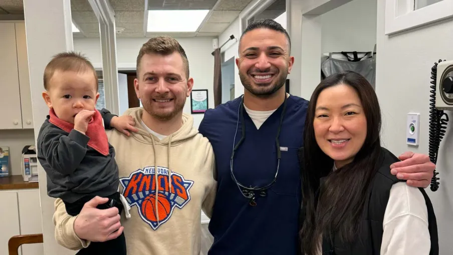 Smiling diverse family and healthcare professional posing together in a medical office hallway.