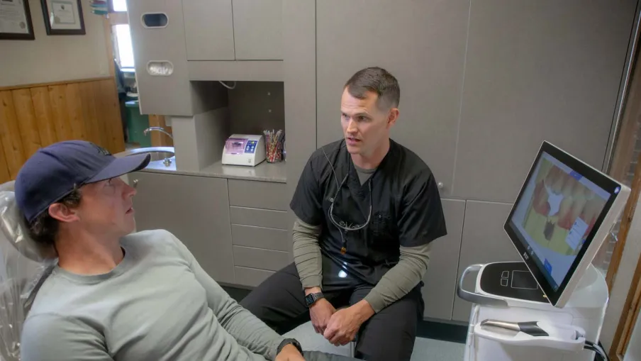 Dentist consulting a male patient in a dental clinic with digital imaging on screen.