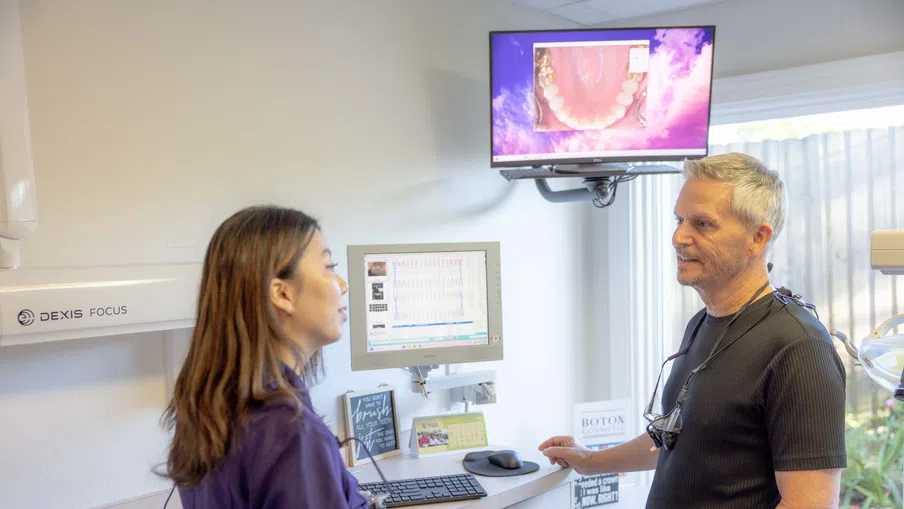 Dentist consulting with patient in dental office with computer screens showing dental images and charts.