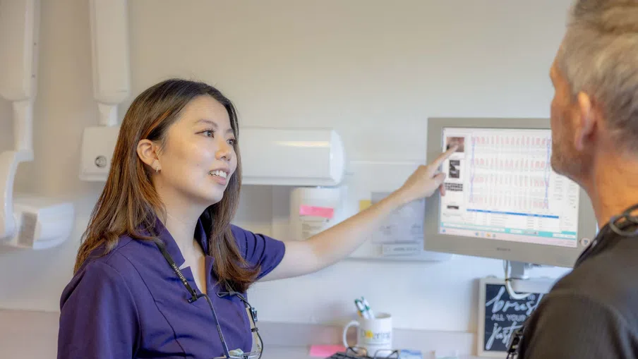 Female dental professional explains X-ray results to male patient using computer screen in clinic