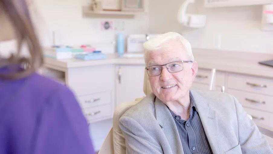 Senior man smiling and talking with medical professional in bright clinic room.