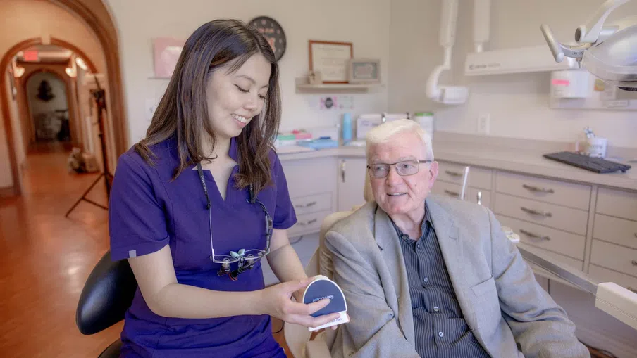 Female dentist explaining dental care to elderly male patient in a bright clinic room.