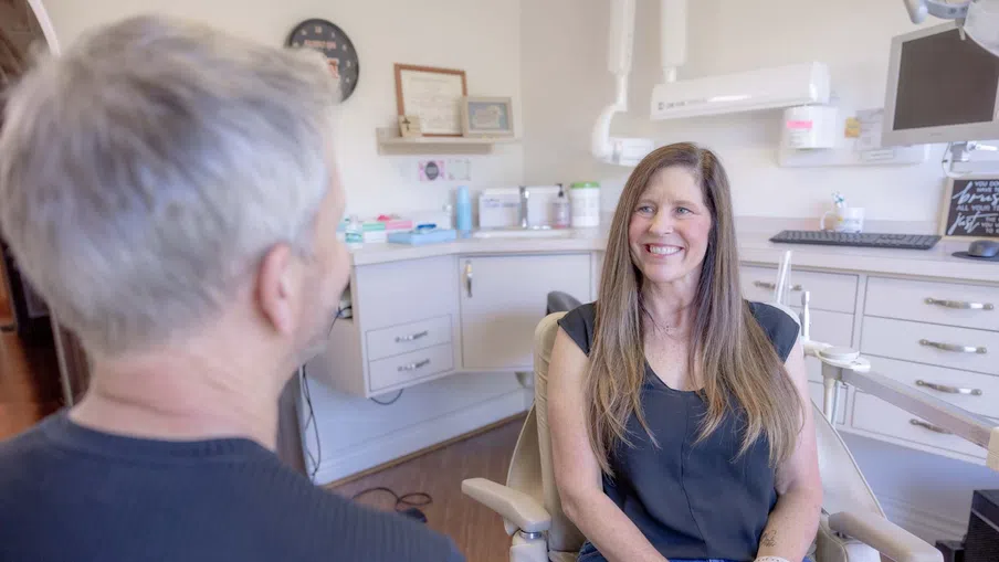 Smiling woman sitting in a dental chair talking to a male dentist in a modern dental office.