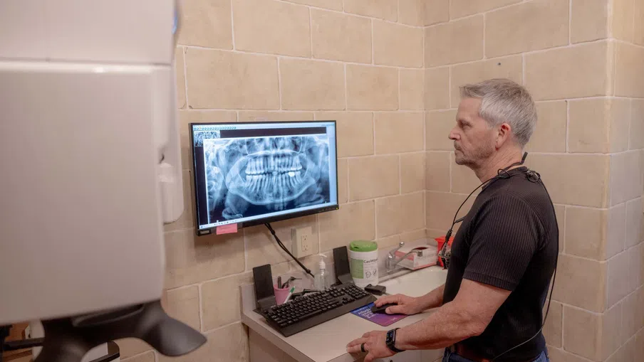 Dentist reviewing a digital dental X-ray on a monitor in a tiled examination room.