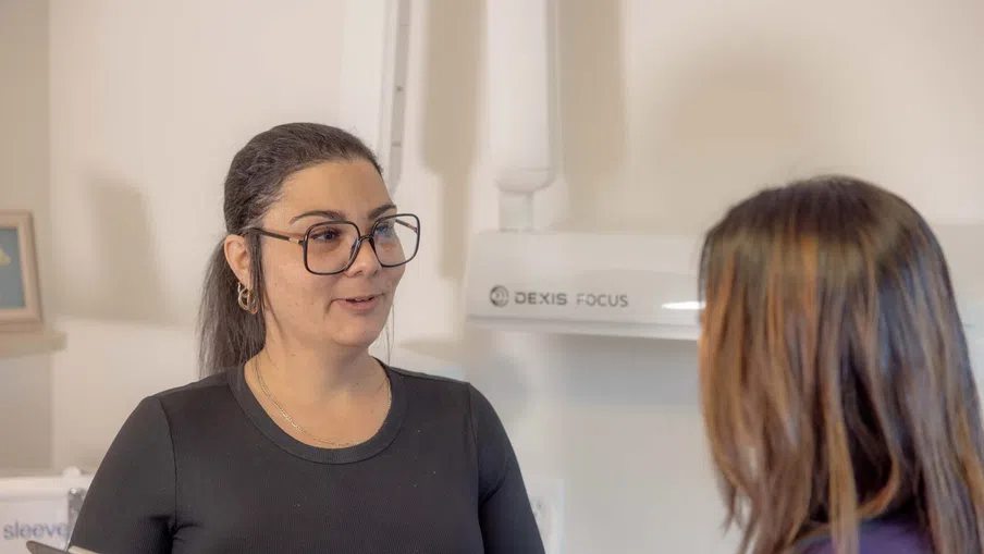 Female healthcare professional wearing glasses talking to a patient in a dental or medical office setting.
