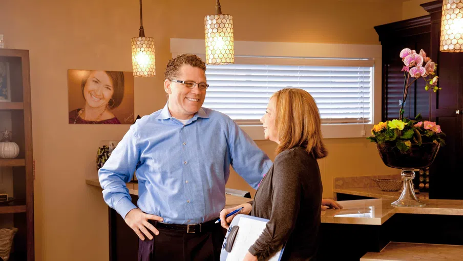 Man and woman engaged in a friendly conversation in a warmly lit modern kitchen.