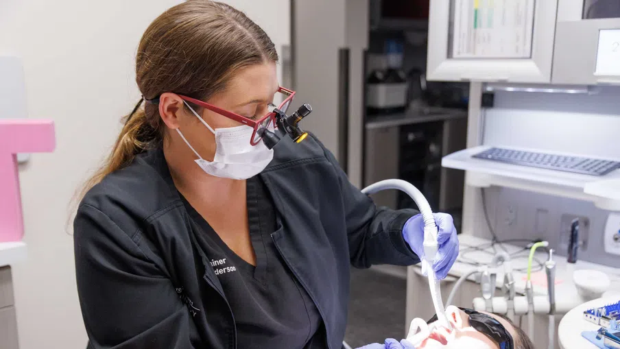 Dentist explaining dental X-ray results to patient showing teeth and roots on a monitor in clinic.