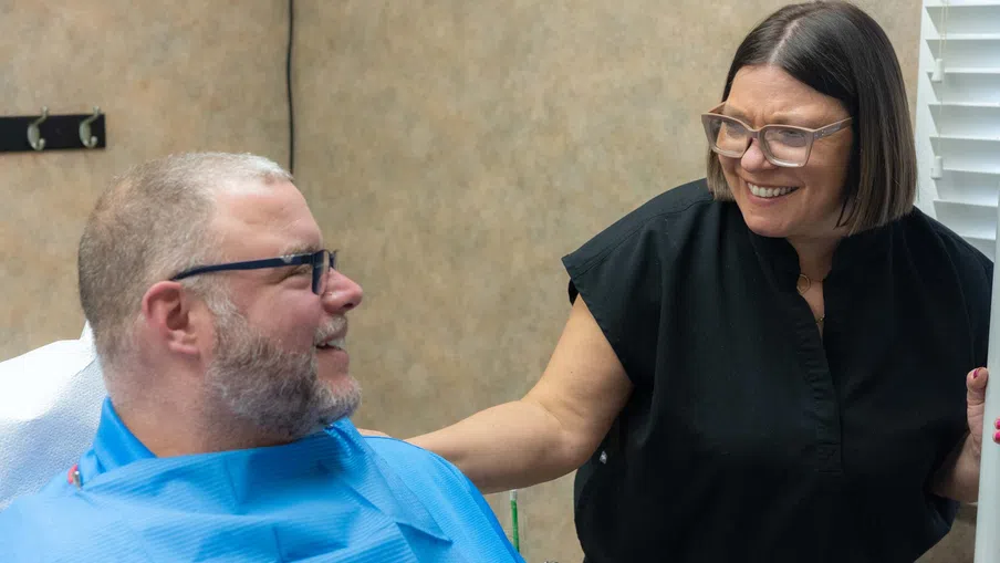 Smiling dental professional interacting warmly with seated male patient in dental office setting.