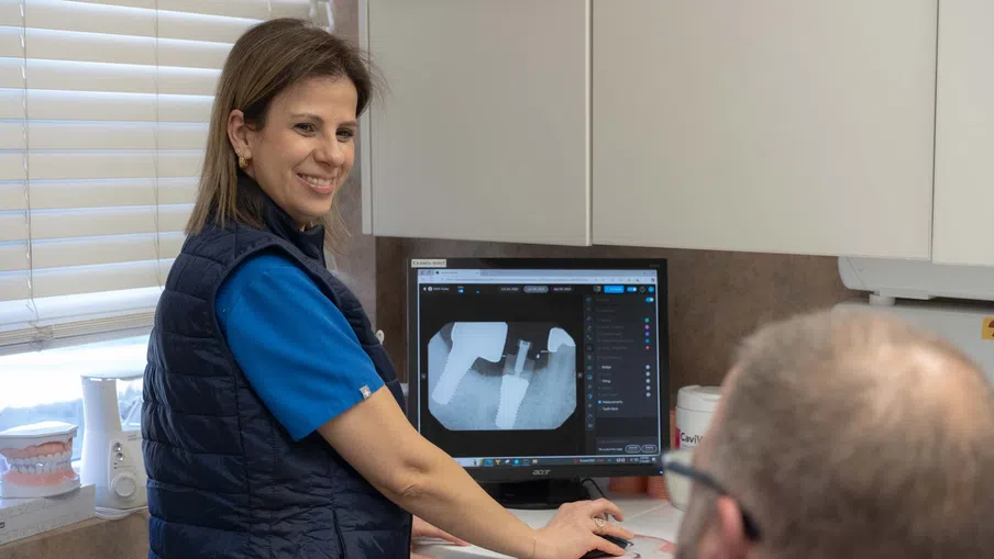 Dentist showing a dental X-ray on a computer to a patient in a dental office with dental models nearby.