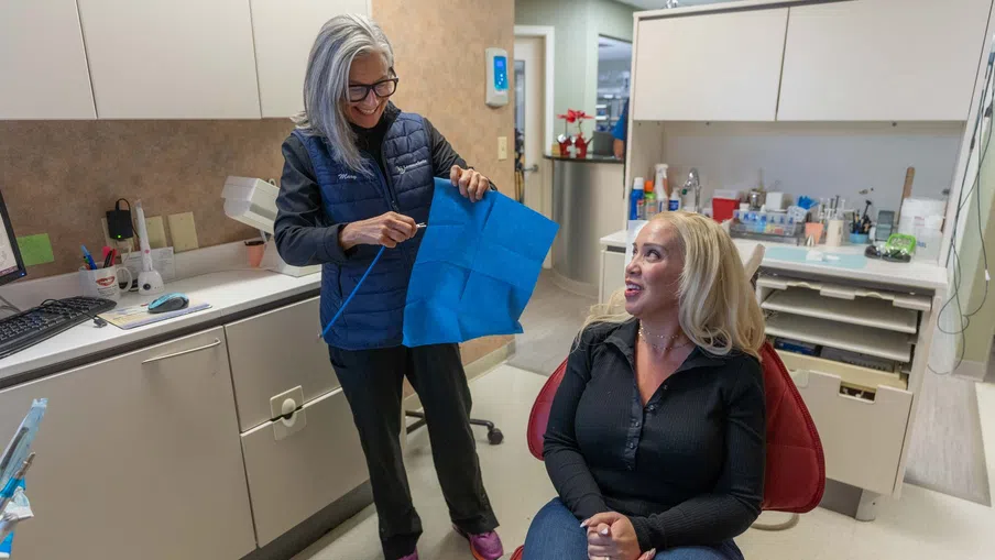 Dentist showing dental bib to seated female patient in bright dental office during consultation