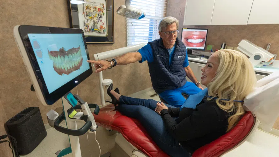Dentist shows digital 3D dental scan to smiling female patient in modern dental clinic consultation.