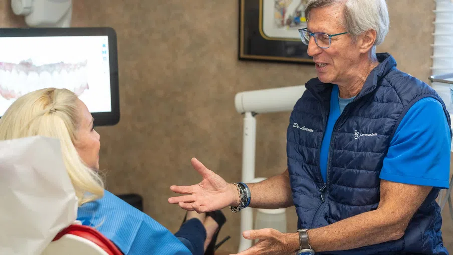 Doctor consulting a female patient in a dental office with a dental X-ray on the screen behind.