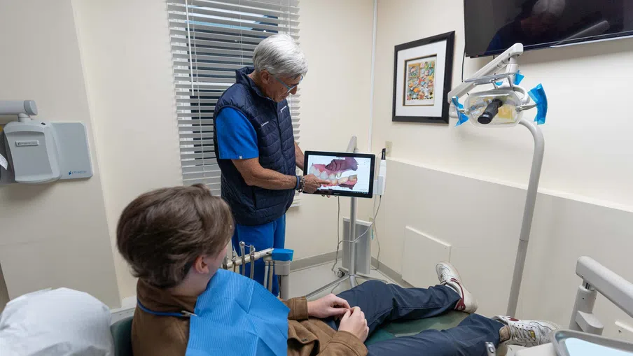 Dentist showing young patient a 3D dental scan on a tablet in a modern dental office room.