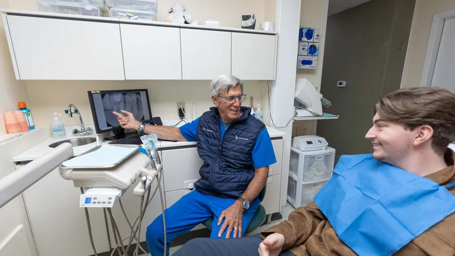 Senior male dentist explaining dental X-ray results to a young male patient in a modern dental clinic.