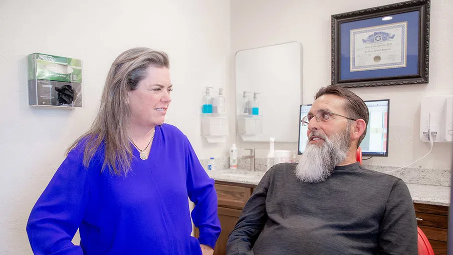 Female healthcare professional in blue blouse consulting male patient with gray beard in medical office
