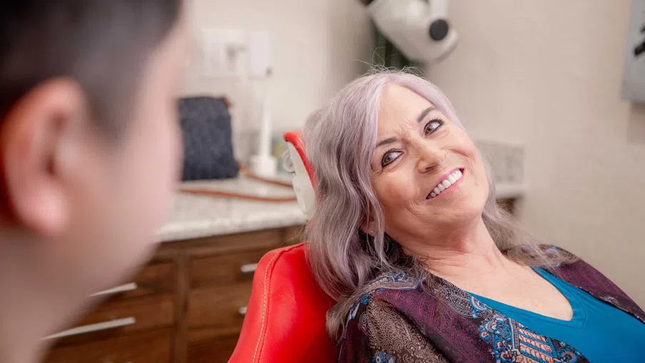 Smiling elderly woman sitting in a red dental chair during a consultation with a dentist.