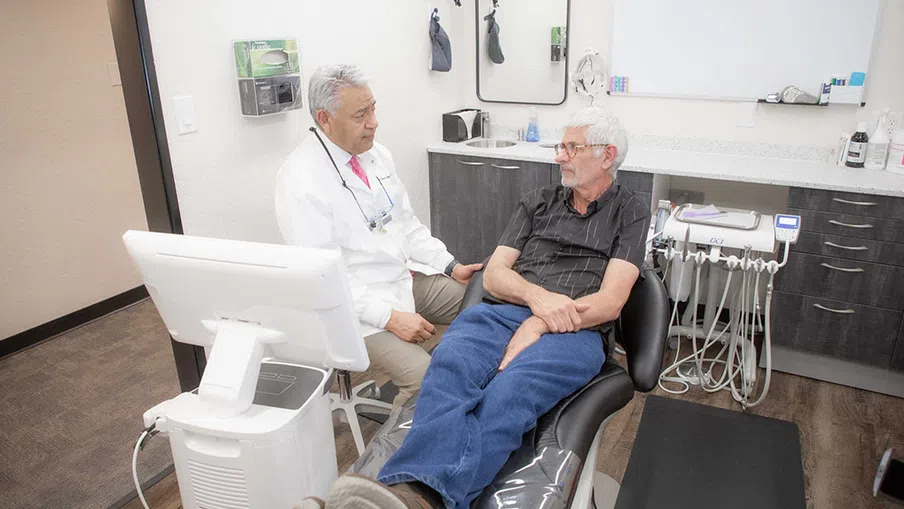Dentist consulting with an elderly male patient seated in a dental chair in a modern clinic room.