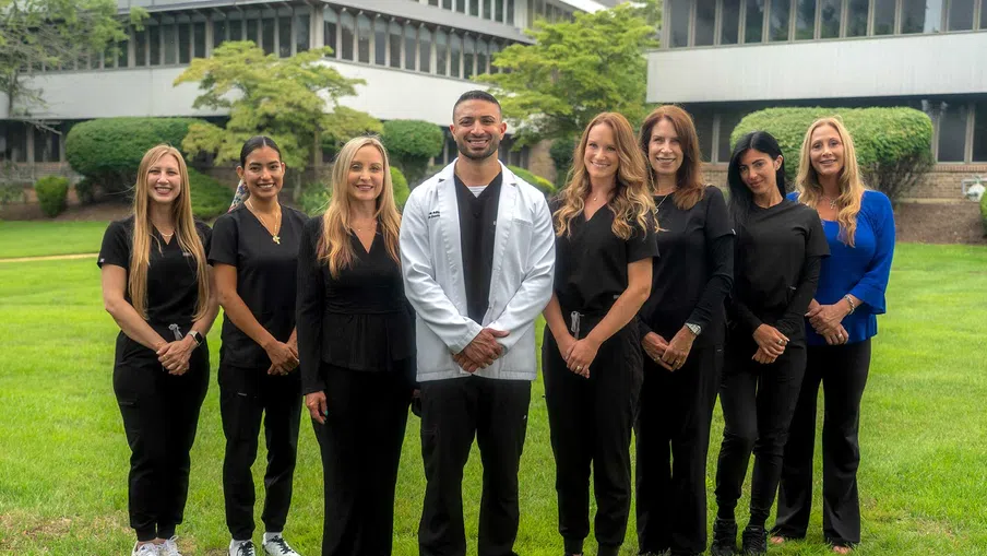 Group of eight medical professionals standing outdoors on grass in front of a modern building, smiling at camera.