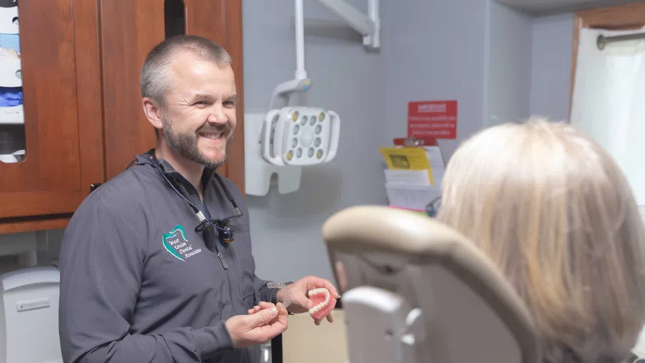 Dentist smiling and explaining dental model to patient in a modern dental clinic room.