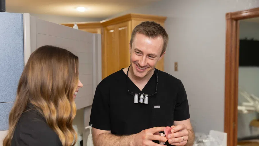 Dentist in black scrubs discussing dental model with female patient in clinic setting.