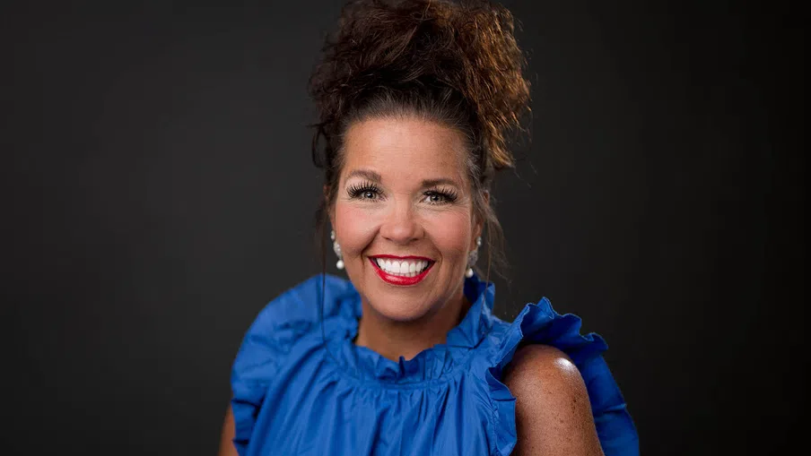 Smiling woman with curly hair in a blue ruffled blouse against a dark background