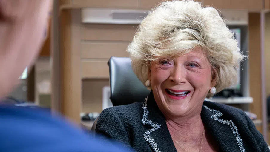 Smiling elderly woman with styled blonde hair chatting in a modern office setting.