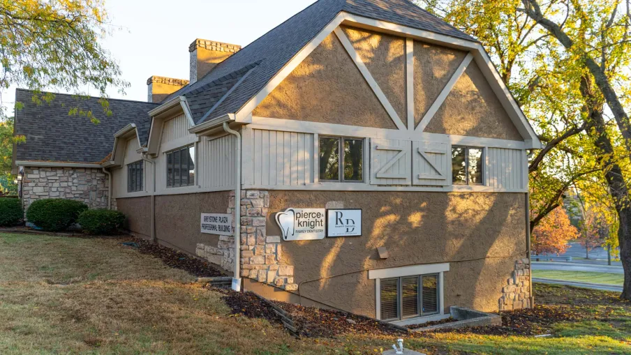 Exterior of a dental office building with stone and siding facade surrounded by grass and trees in autumn light