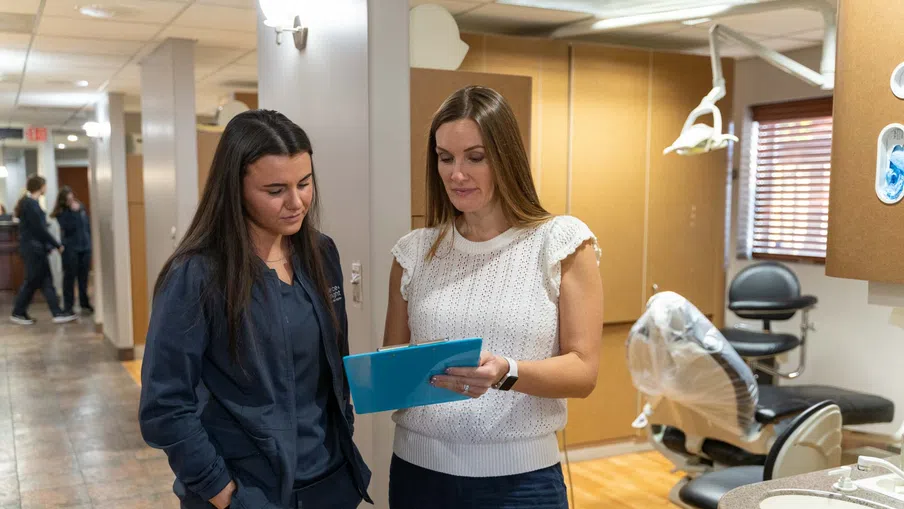 Dentist and patient review dental records together in a modern clinic hallway near treatment rooms.