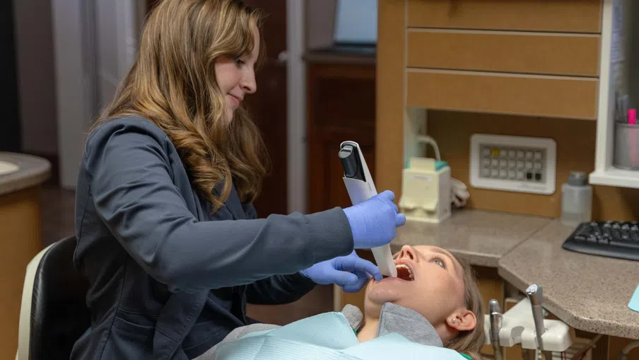 Dental professional using an intraoral scanner on a female patient in a dental office examination.