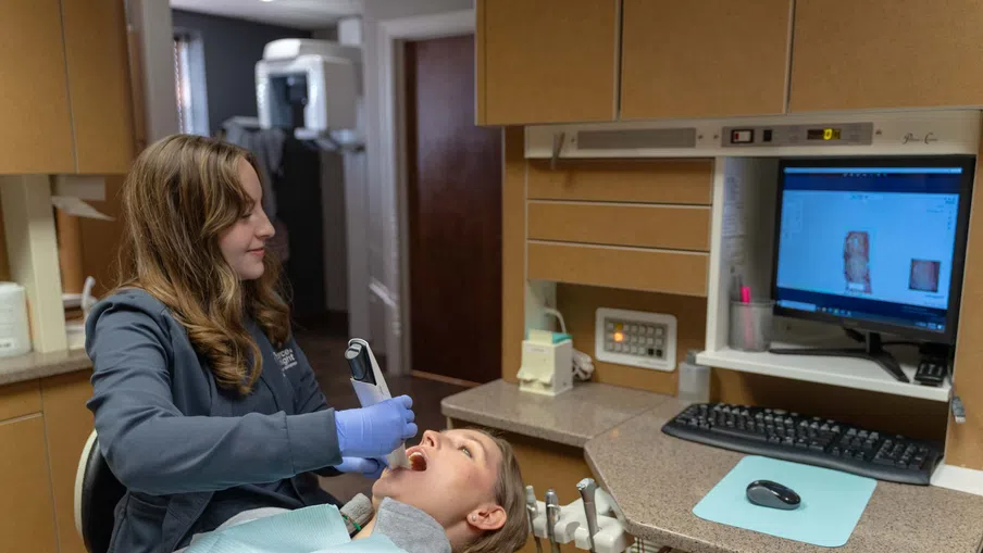 Dentist using digital scanner to examine patient's teeth in modern dental office with computer display.