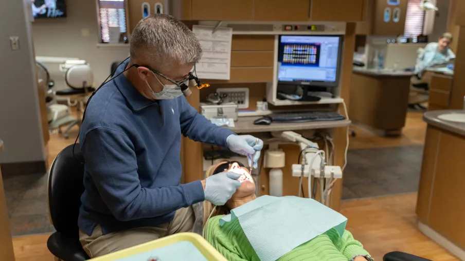 Dentist wearing mask and gloves treating a patient lying in dental chair in modern clinic.