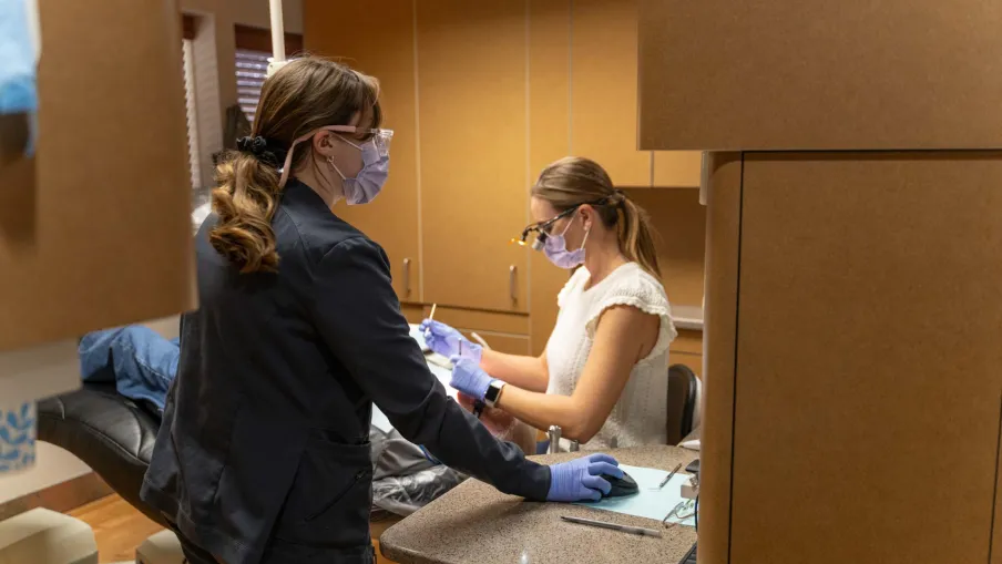 Dentist wearing mask and gloves treating patient in modern dental clinic with protective barriers