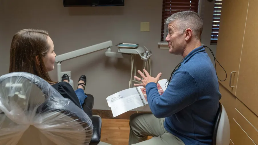 Dentist explaining dental treatment plan to patient in clinic with dental equipment visible