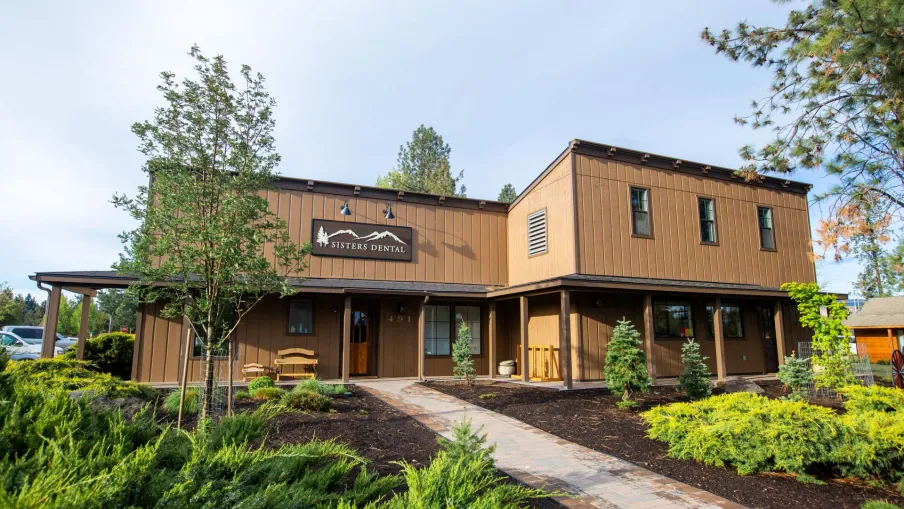 Modern brown two-story dental office building with surrounding greenery and clear sky background.