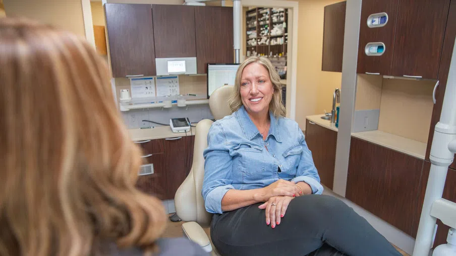 Smiling woman sitting in a dental chair during consultation with a dental professional in modern clinic.