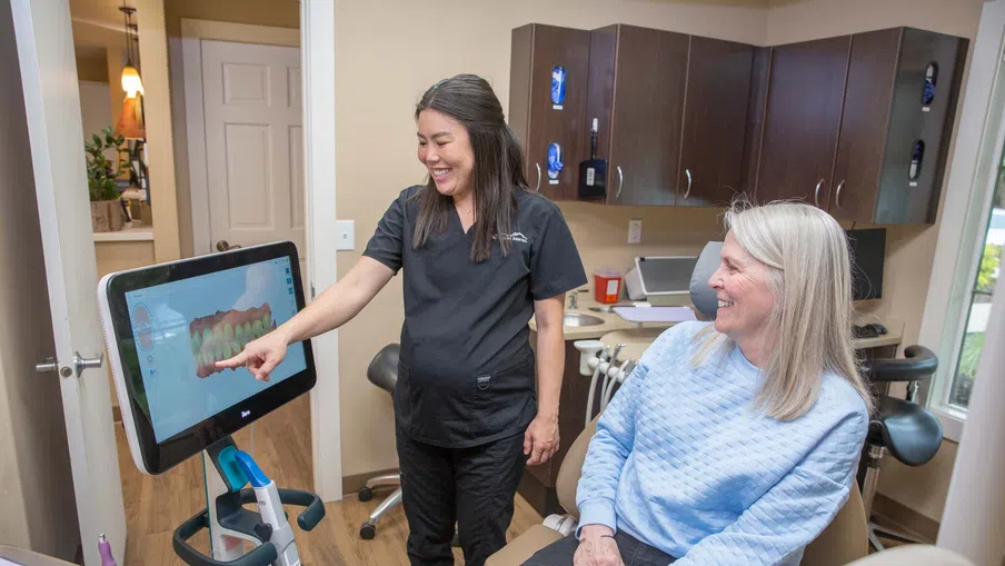 Dentist showing digital dental scan to smiling senior woman in dental office consultation.