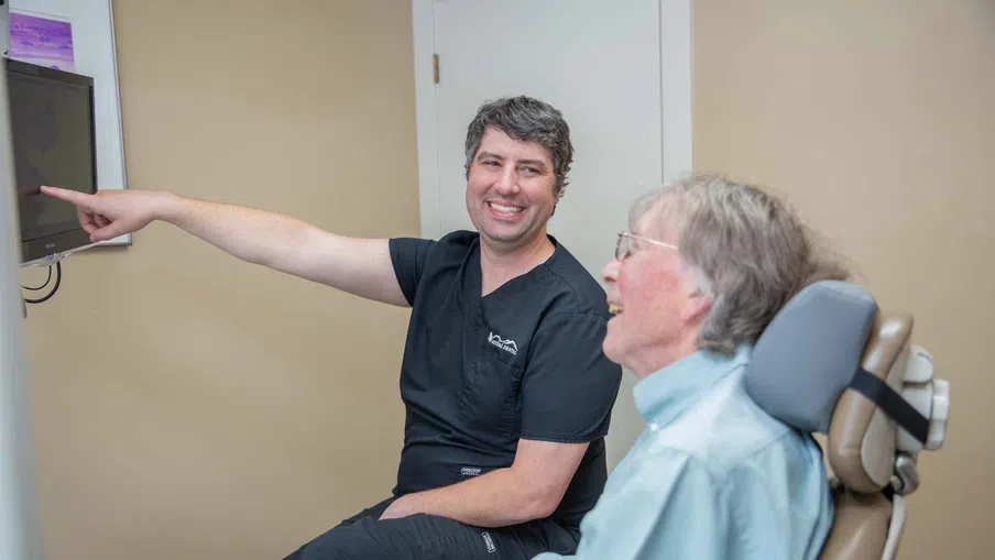 Smiling dentist explaining dental X-ray on monitor to elderly male patient in dental office