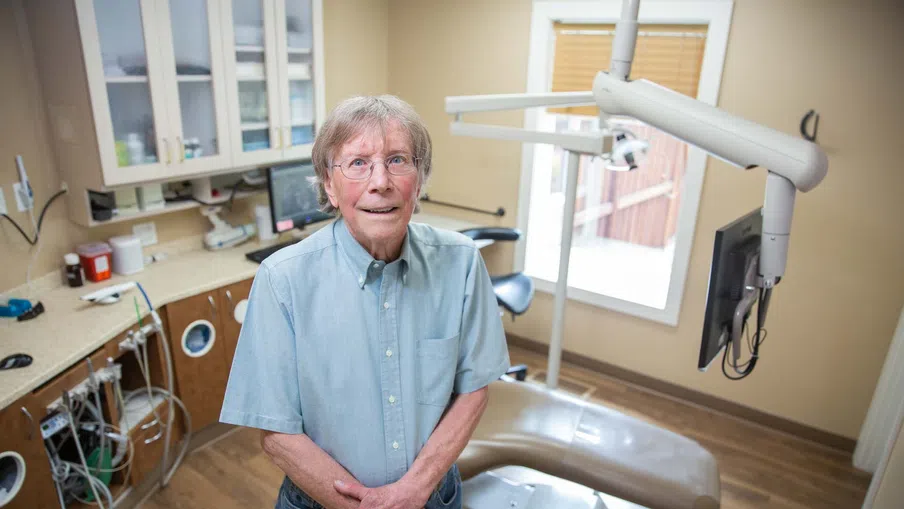 Senior man standing in a modern dental office with dental chair and equipment in the background
