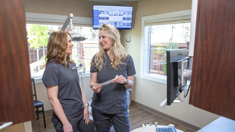 Two female dental professionals discussing patient records in a modern dental office with digital X-rays on screen