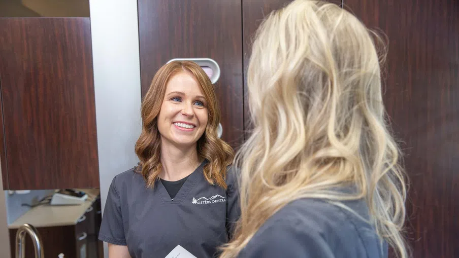 Two dental professionals in gray scrubs discussing a patient file in a dental office.