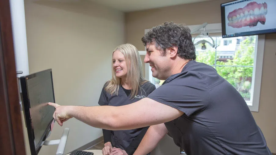 Two dental professionals reviewing dental images on a computer screen in a bright clinic room.