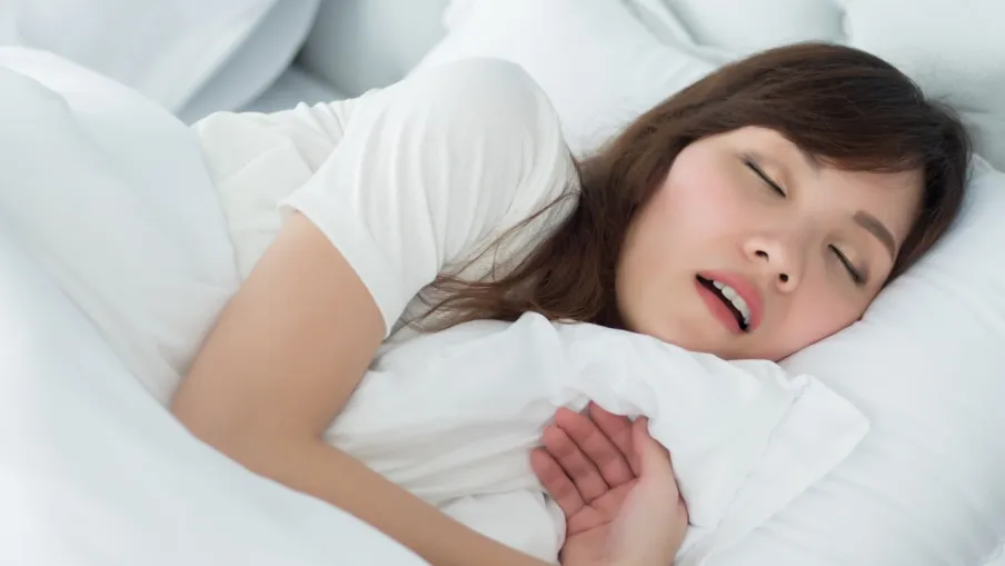Woman sleeping peacefully on white bed hugging a pillow with relaxed expression and closed eyes