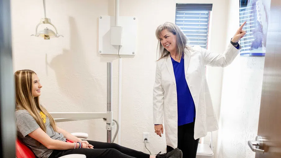 Female dentist showing a dental X-ray to a young female patient sitting in a dental chair smiling.