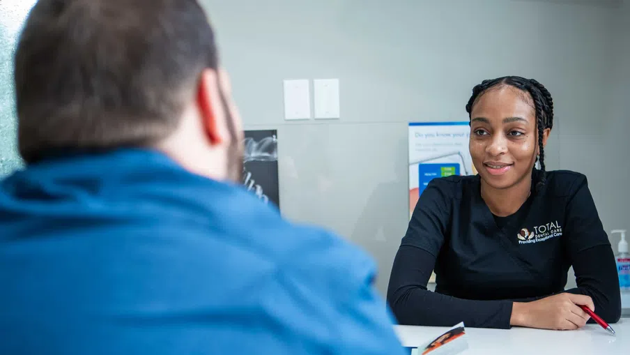 Healthcare worker in uniform consulting with a patient across a white desk in a clinic setting.