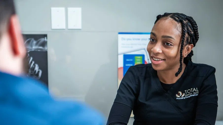 Dental professional in black scrubs consulting a patient in a bright clinic setting.