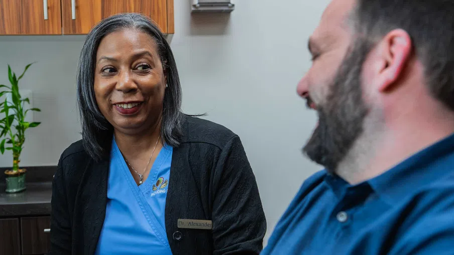 Female doctor smiling and talking to a male patient in a medical office with a plant in the background