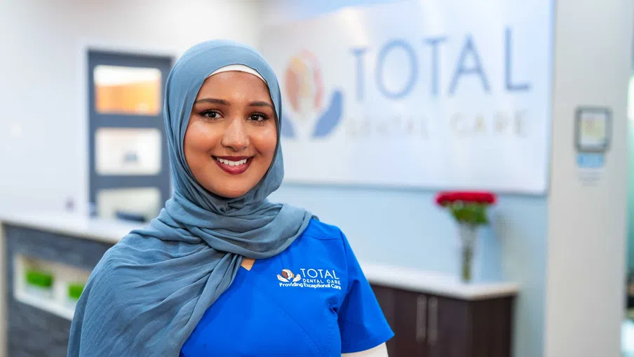 Smiling female dental professional in blue scrubs and hijab at Total Dental Care clinic reception area